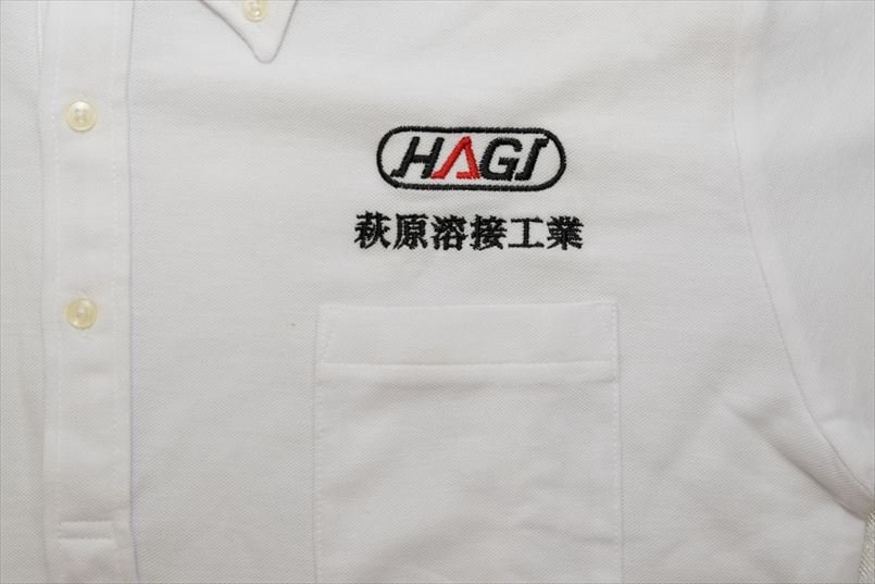 左胸に赤と黒の糸を使い、「HAGI」をアレンジしたロゴマークと社名を刺繍